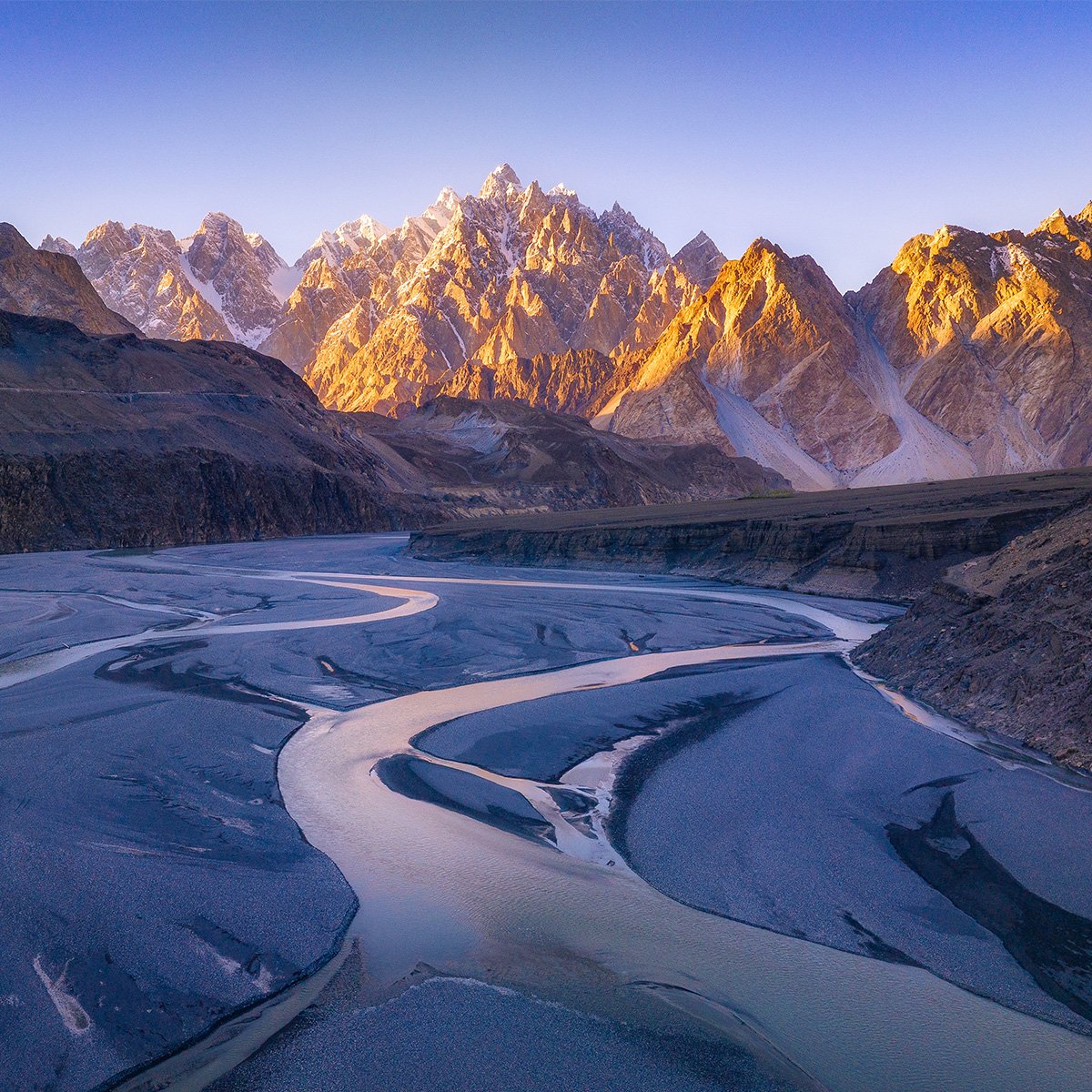 Un paysage serein de montagne avec un sommet enneigé se reflétant dans un lac calme sous un ciel bleu clair et quelques nuages.