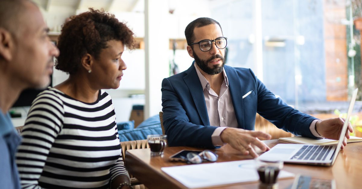 A businesswoman and businessman engage in a professional meeting at their office, surrounded by their adult team.