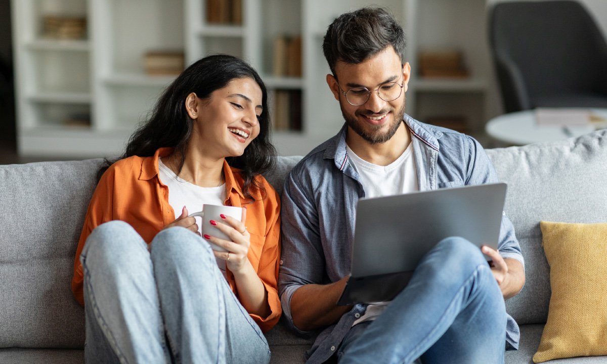 Man and woman sitting on couch looking at laptop