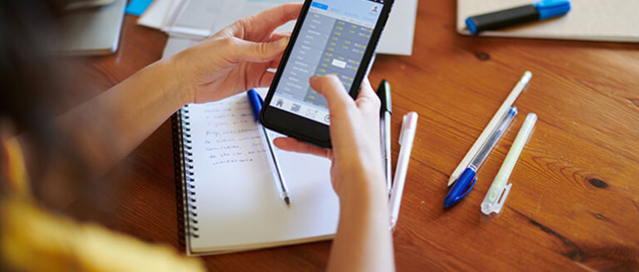 Student sitting at her desk with a notepad and pens while using her phone