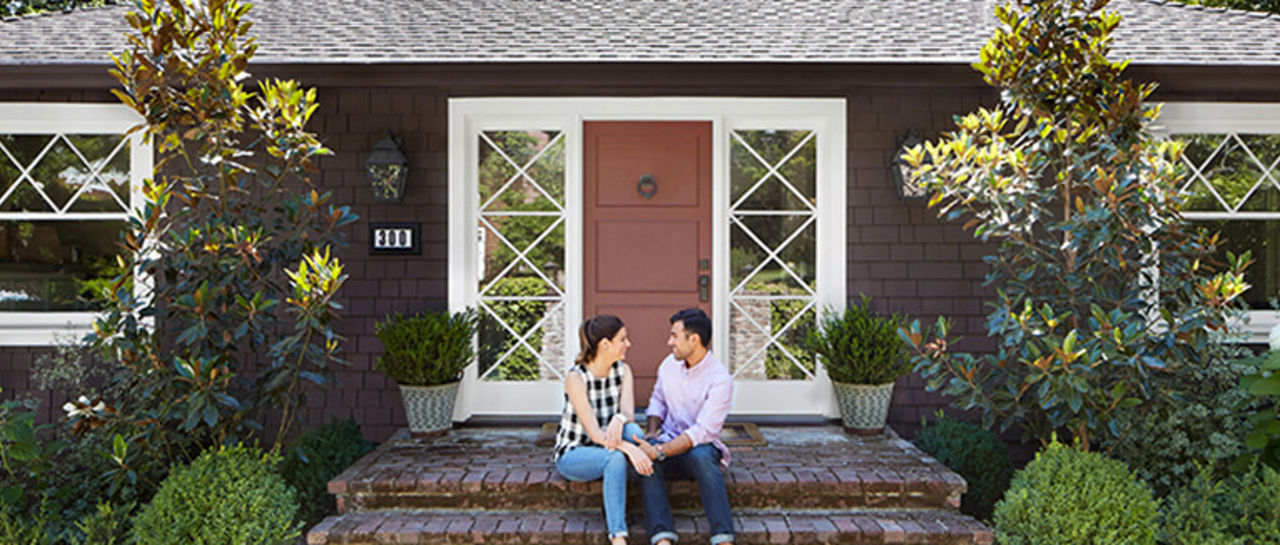 Young couple sitting on the front steps of the home they purchased together