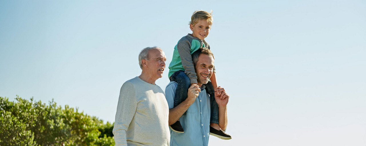 A young boy sitting on his fathers shoulders with his grandfather on a beach