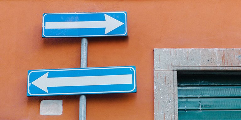 Two blue arrow signs pointing in opposite directions against a bright orange wall 