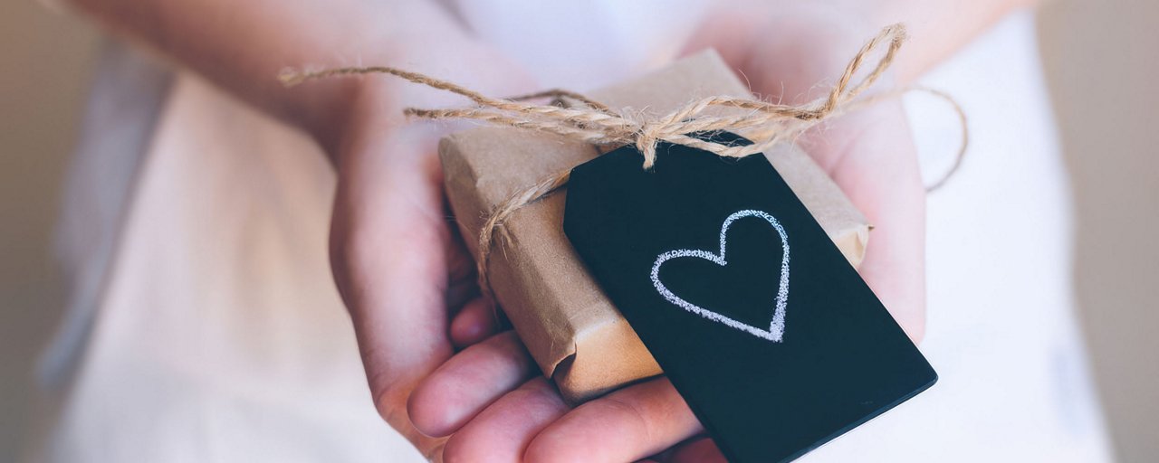 Woman holding a present wrapped in brown paper with a black tag with a white heart on it