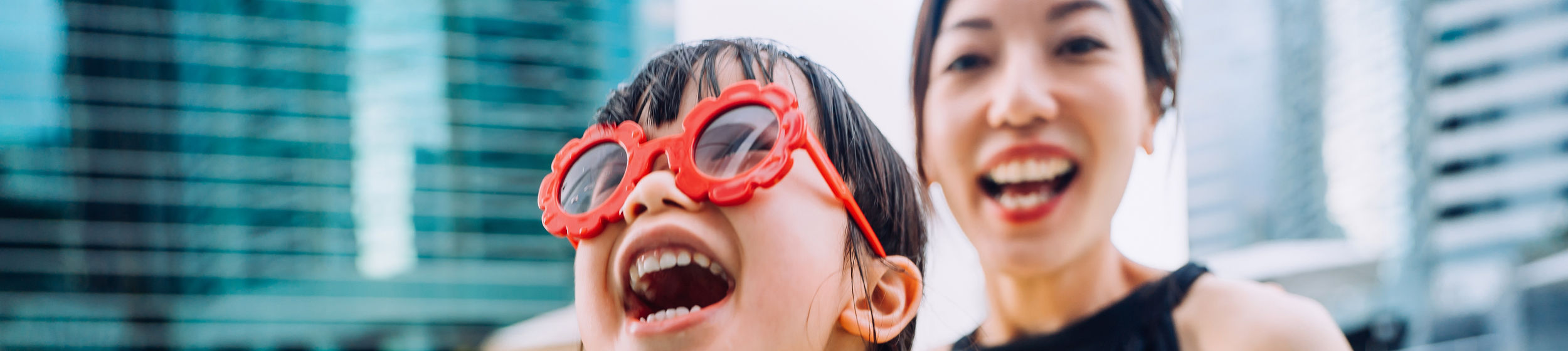 Happy little Asian girl with sunglasses smiling joyfully and enjoying family bonding time with mother, having fun in the swimming pool on Summer vacations