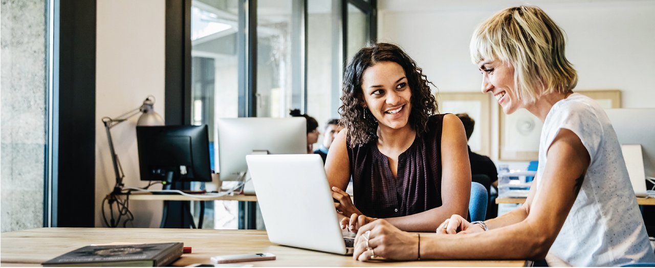 A focused young businesswoman is diligently working on her laptop in a modern office environment.