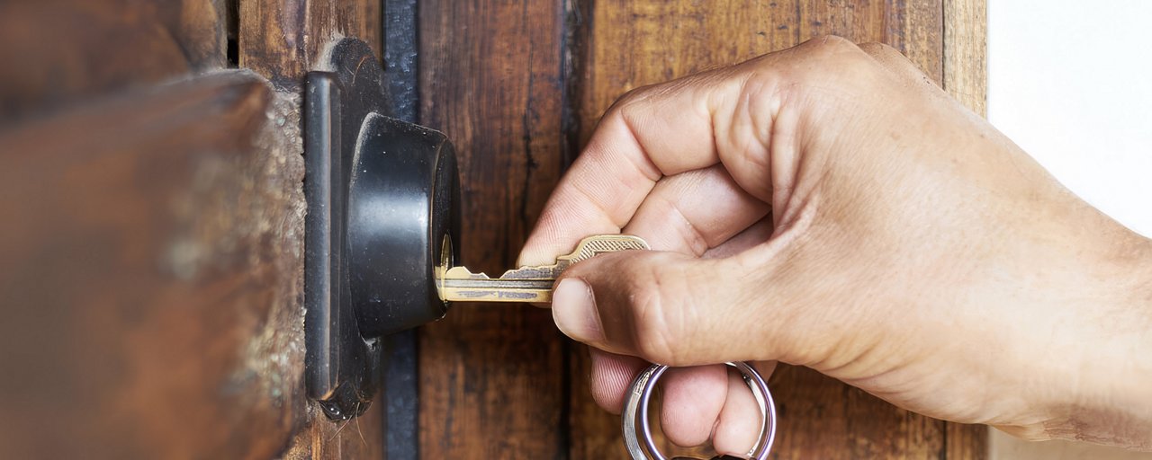 A man inserting a key into the lock of a wooden front door to a house