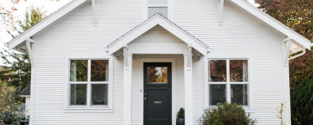 White wooden house with a black painted front door in the fall foliage 
