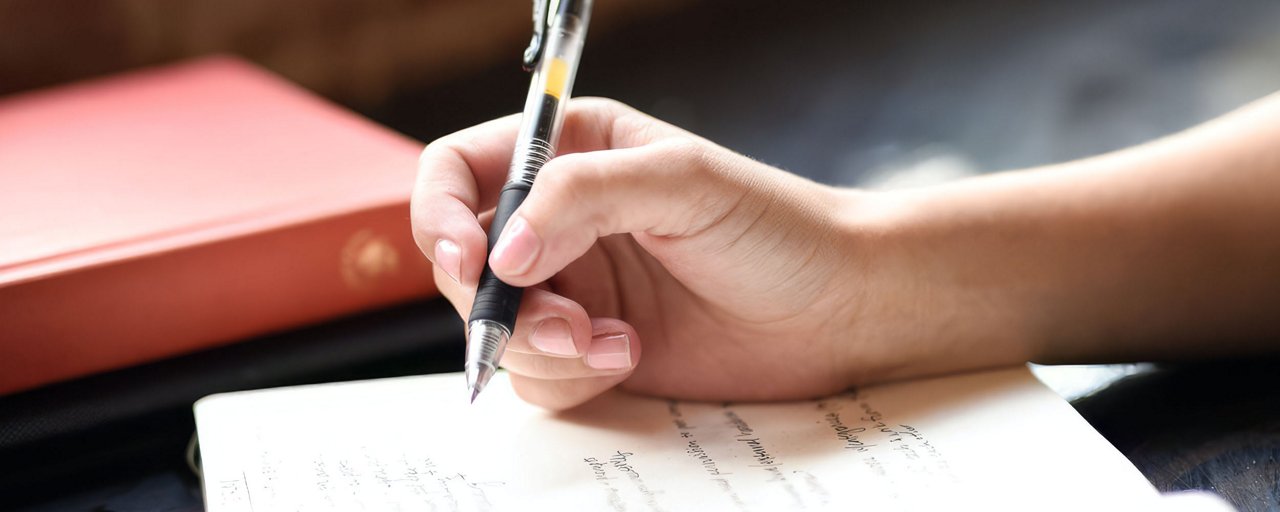 Close up of a woman writing in a journal next to a stack of books