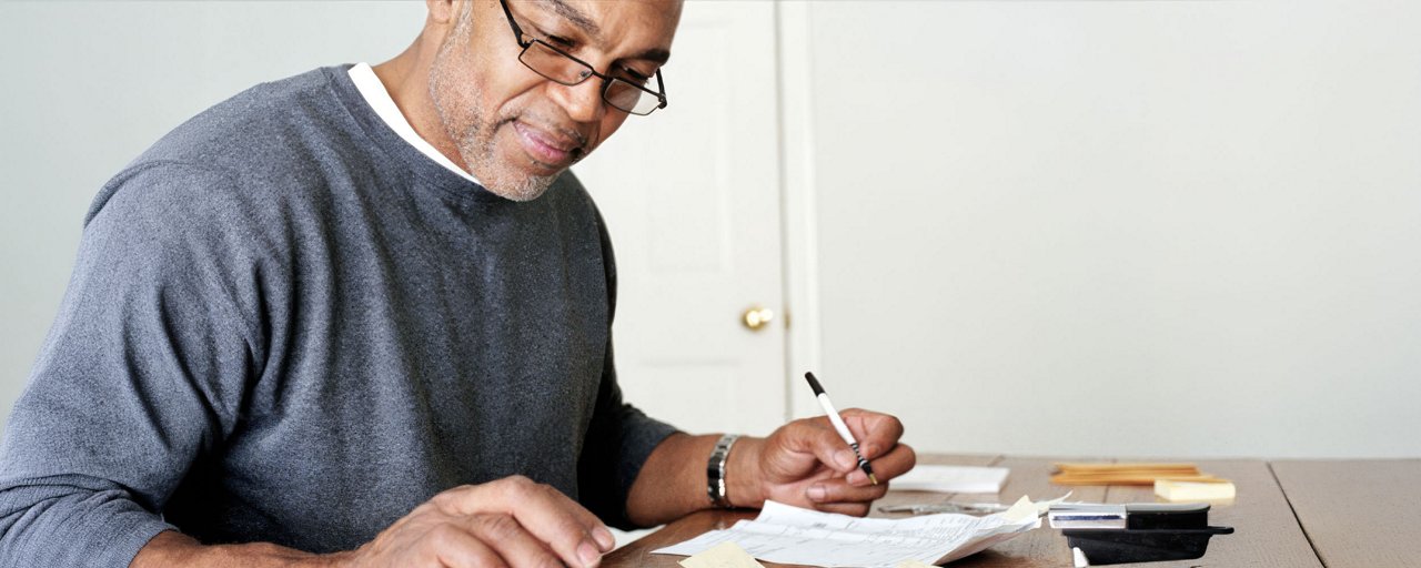 A middle-aged man doing his expenses with his receipts and a calculator on his desk 