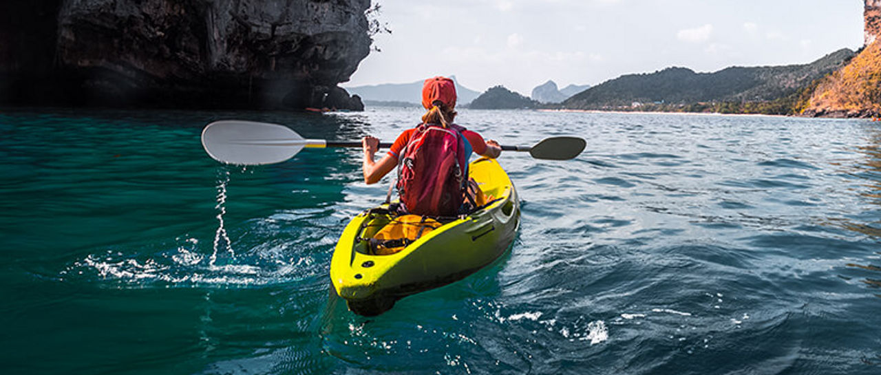 A woman wearing red paddling a yellow kayak in open waters surrounded by islands