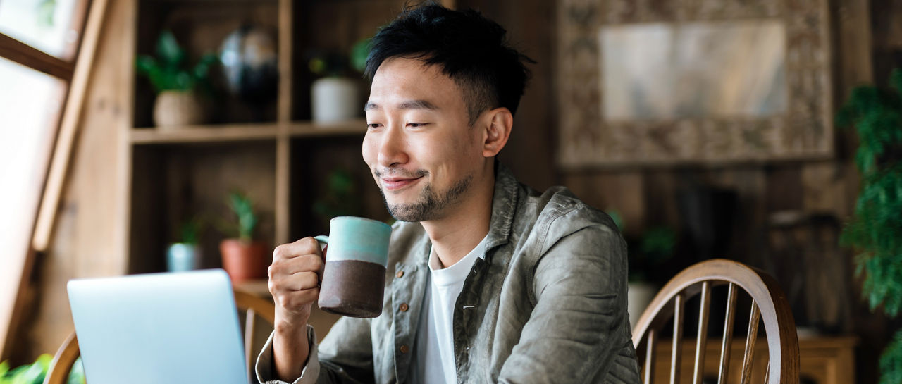 Young Asian man using laptop in the living room. Managing personal banking and investment via online banking. Making financial plan, planning savings and spending, managing online stock trades. E-banking with technology