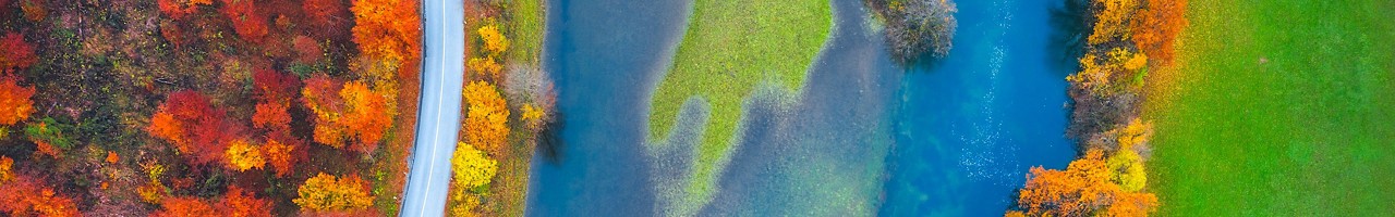 Aerial view on idyllic country road by the river. Mixed forest in autumn colours.