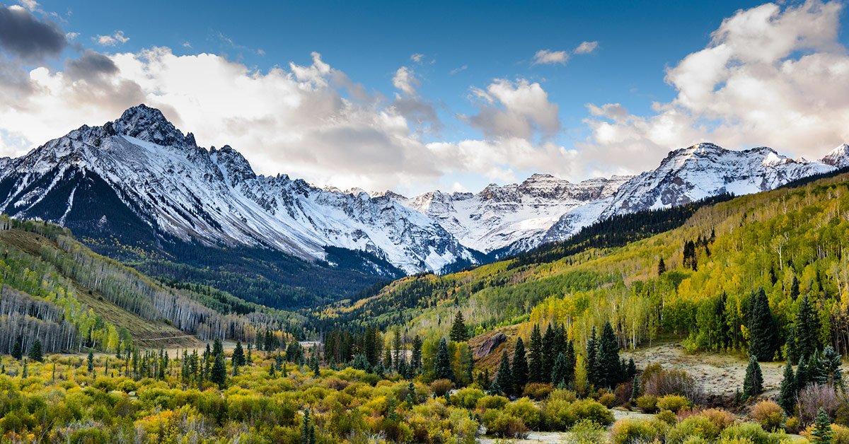 Panoramic view of a broad wooded valley, with snow-capped mountains in the distance.
