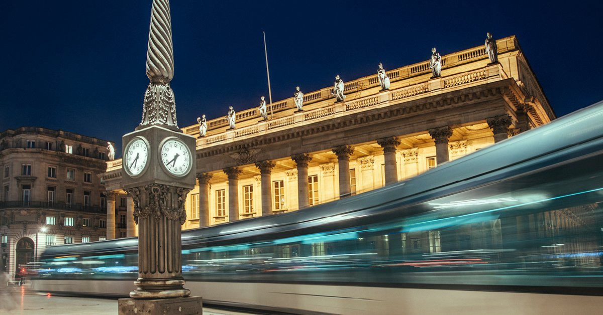 Photo panoramique d'une ville européenne, mise en valeur par une tour horloge proéminente, un bâtiment gouvernemental imposant et somptueux, et un train de métro aérien circulant à grande vitesse.