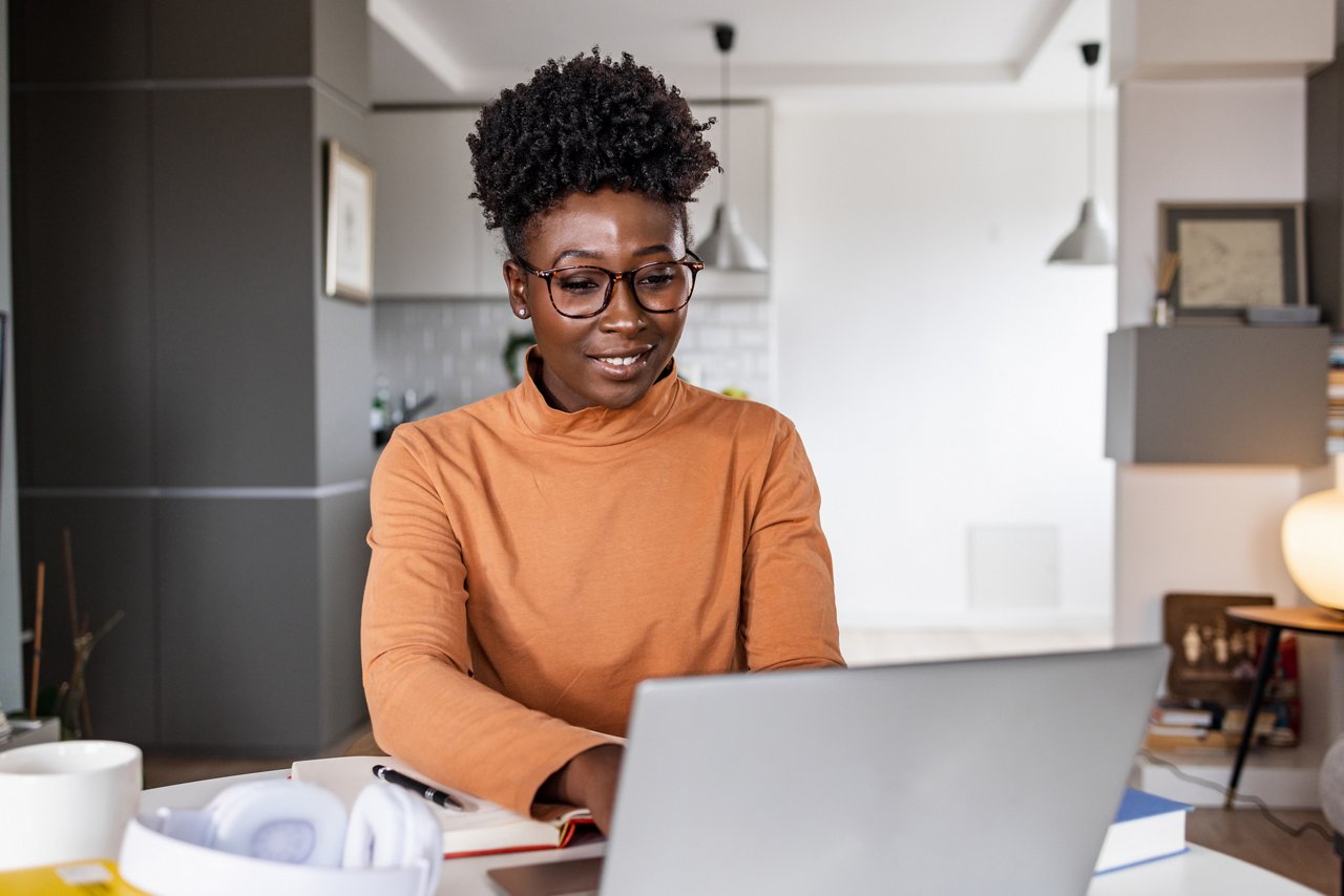 A young African American woman is sitting at the table at home. She is typing on the laptop keyboard. Working atmosphere.