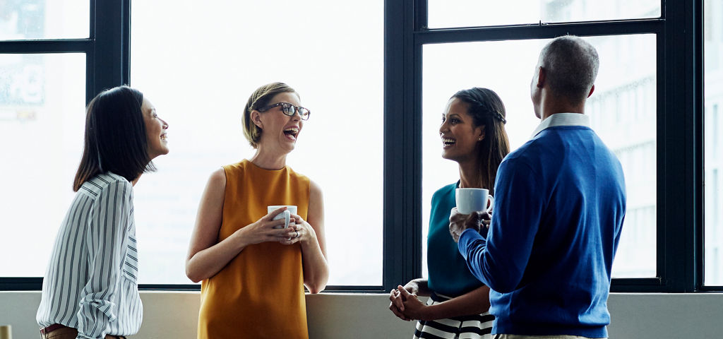 professionals talking in a modern office lounge with large windows and city view.