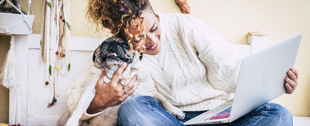A women cuddling her dog and looking at her laptop.