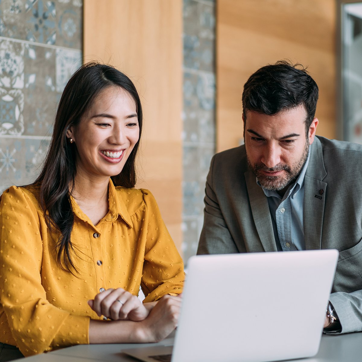 Shot of a two confident business persons sitting on a desk in the office and sharing ideas. Businessman and businesswoman in meeting using laptop and discussing business strategy. Business coworkers working together in the office.