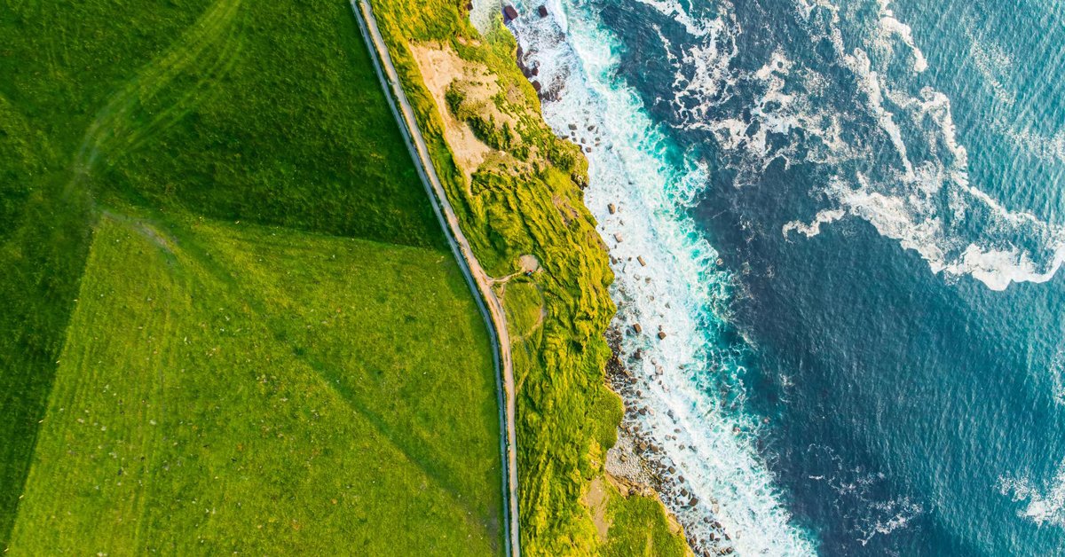 Vue aérienne d'une colline verdoyante et des vagues qui s'écrasent contre une falaise 