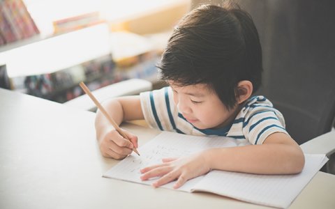 Little Asian child  using a pencil to write on notebook at the desk