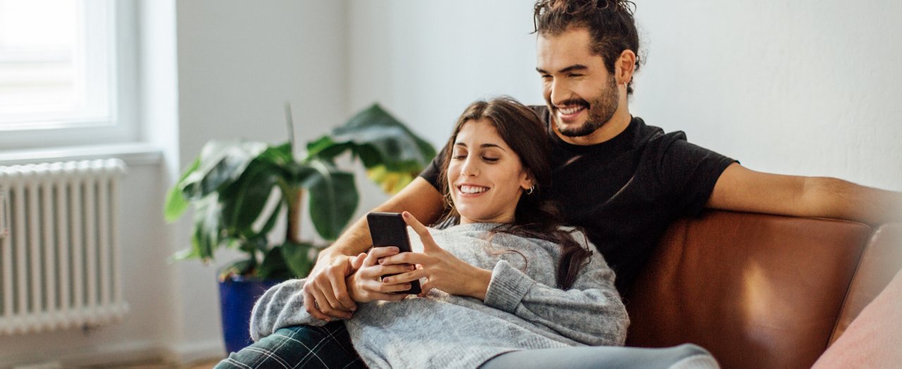 Smiling young couple lounging on the couch, looking at their phone