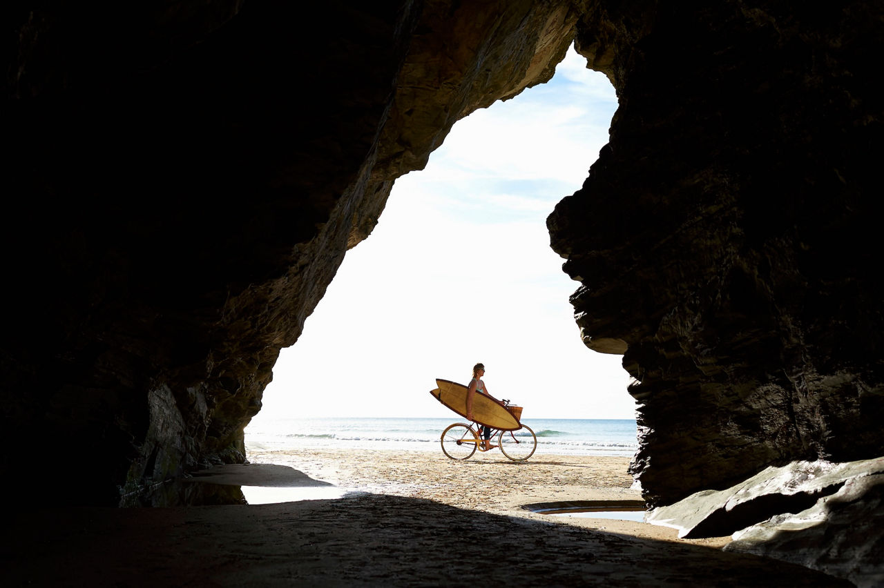 woman Biking on beach with surfboard