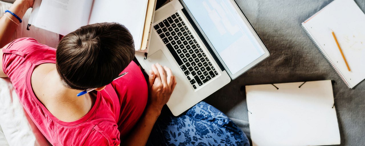 Woman sitting on her couch with her laptop computer, textbooks, and multiple notebooks