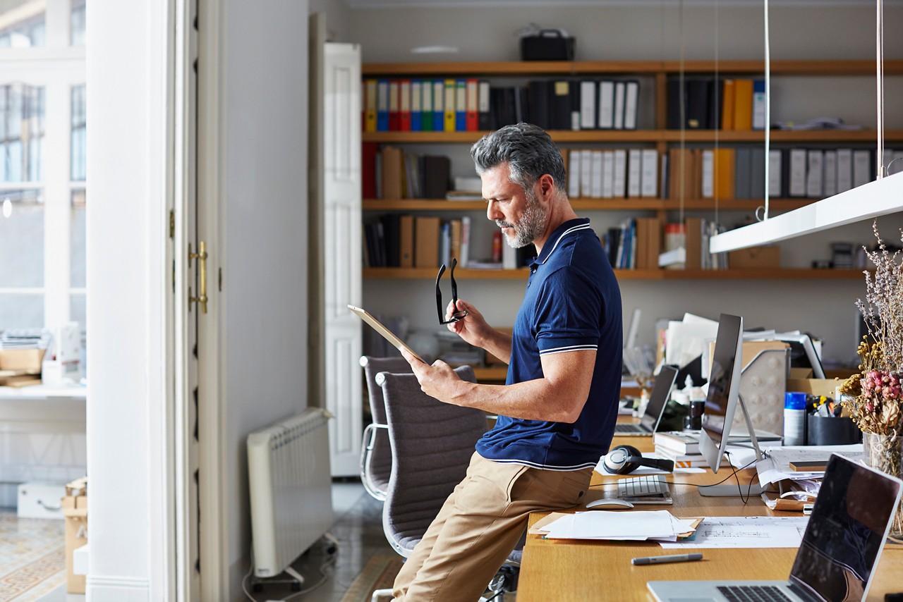 Side view of businessman using digital tablet while leaning on desk in office