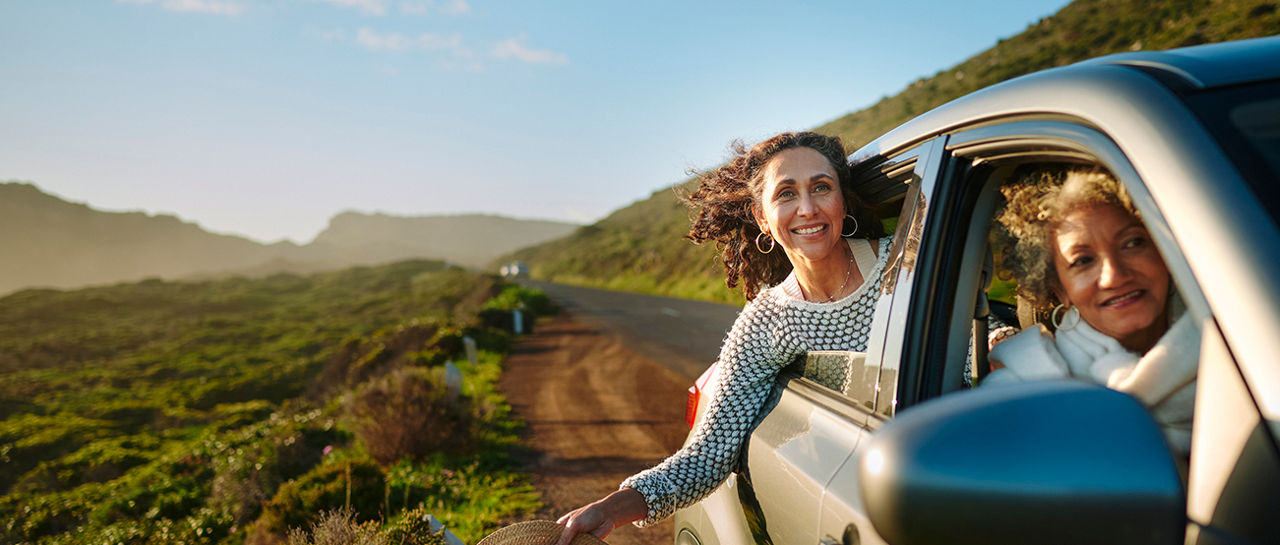 Group of smiling mature female friends looking out at the scenic view through car windows during a summer road trip together