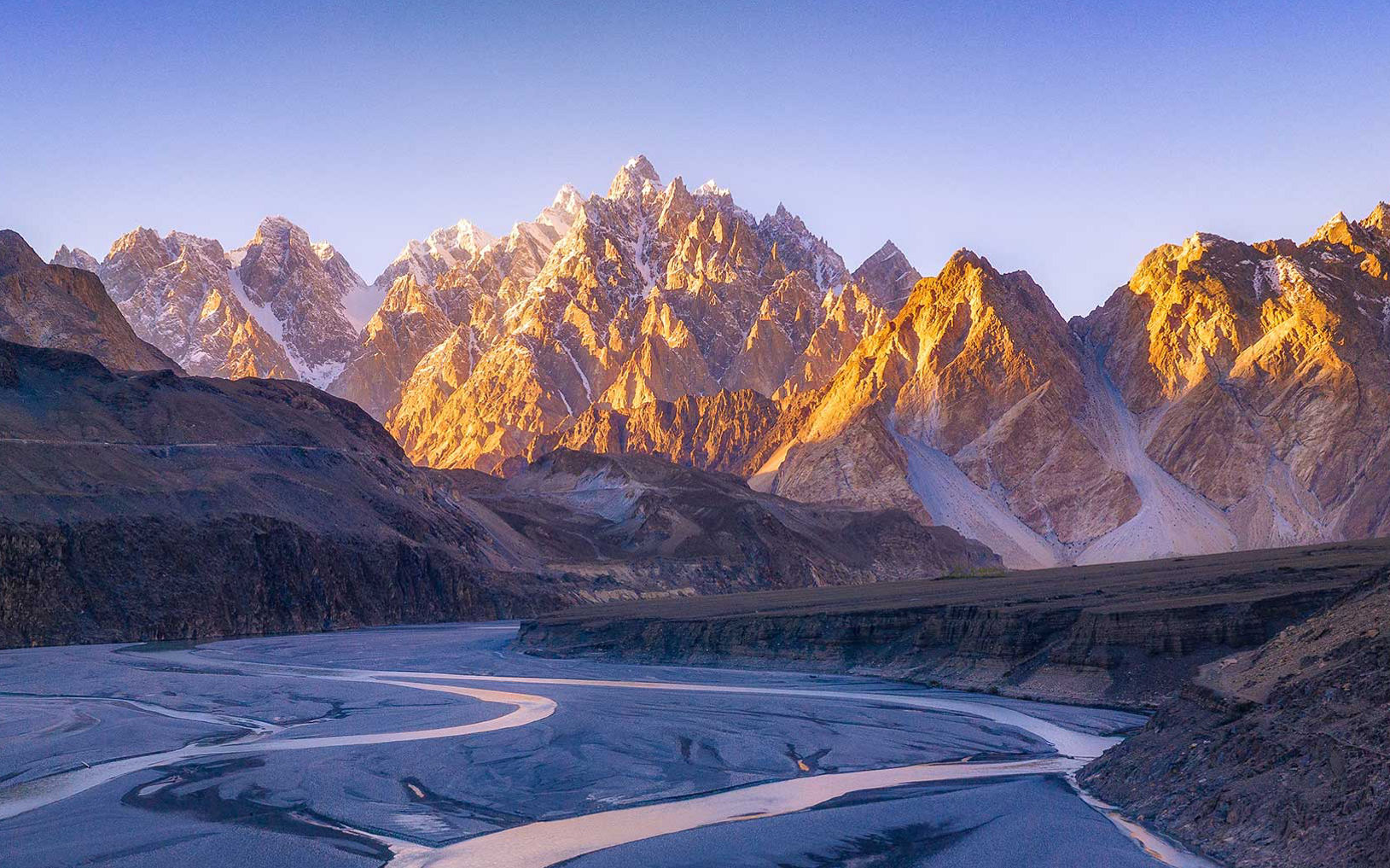 Sunlit mountain peaks rising above a winding river in a rocky valley.