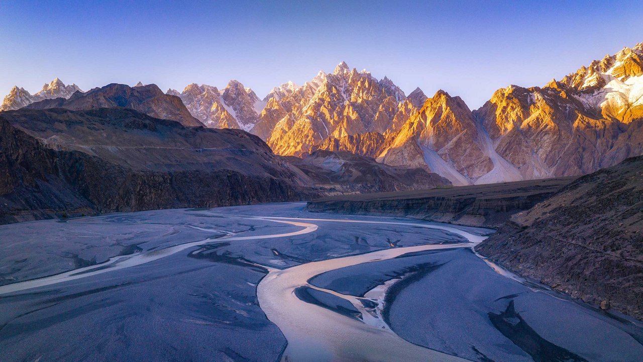 Sunlit mountain peaks rising above a winding river in a rocky valley.