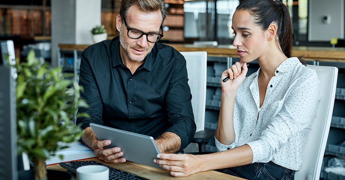 A businessman and a businesswoman, engaged in a professional discussion, are working together on a laptop.