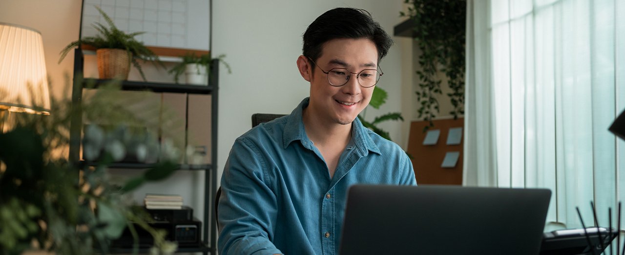 A man wearing glasses is focused on working on his laptop at a desk