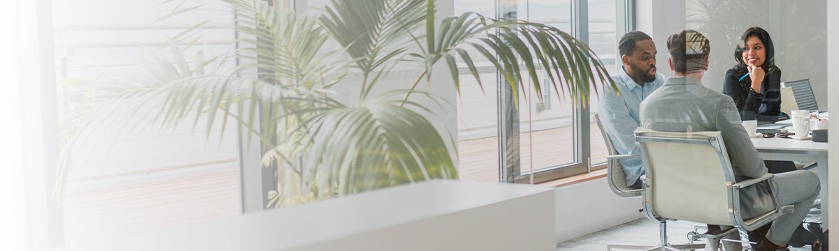 A group of diverse individuals seated around a table in a modern office setting, engaged in discussion.