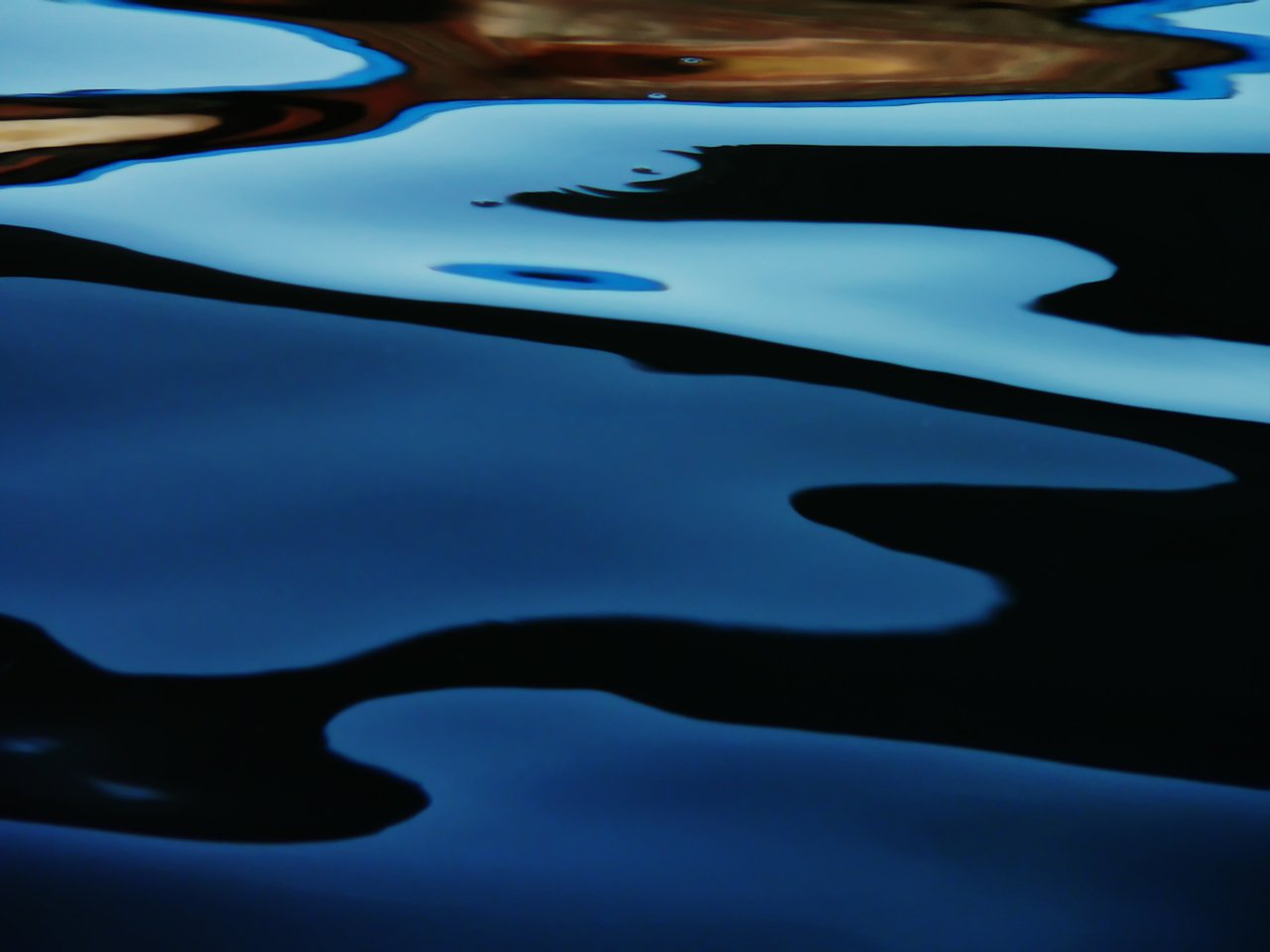 Gros plan abstrait d’eau ondulante présentant des reflets bleu foncé, noir et bleu clair.