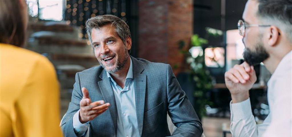 Three people seated in a modern office, engaged in a discussion.ale manager discussing new project with his colleagues. Company owner on a meeting with two of his employees in his office.