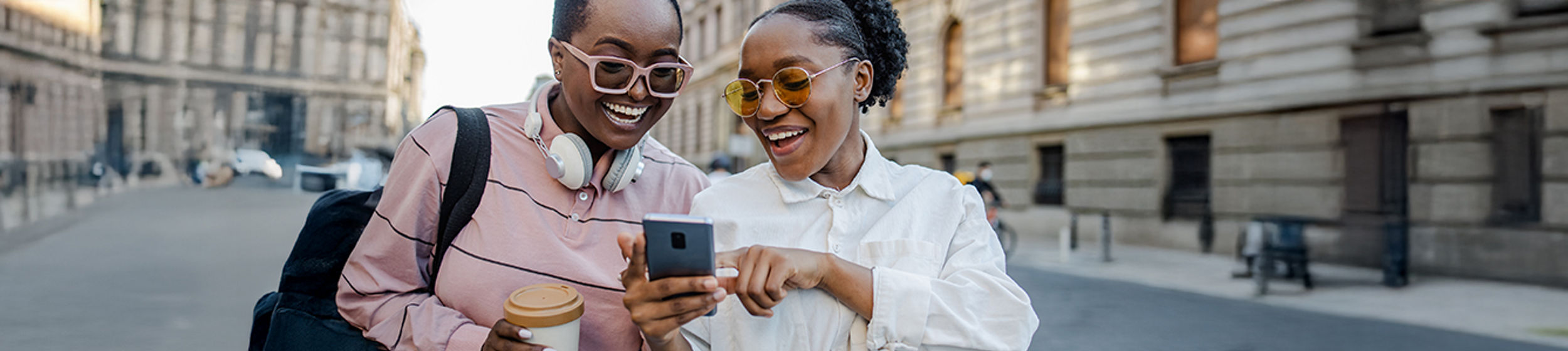 Deux jeunes femmes sourient et regardent un telephone intelligent.