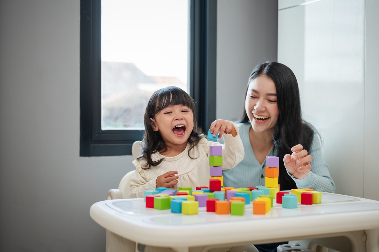 happy toddler girl playing wooden block toy cubes with her mother on a table