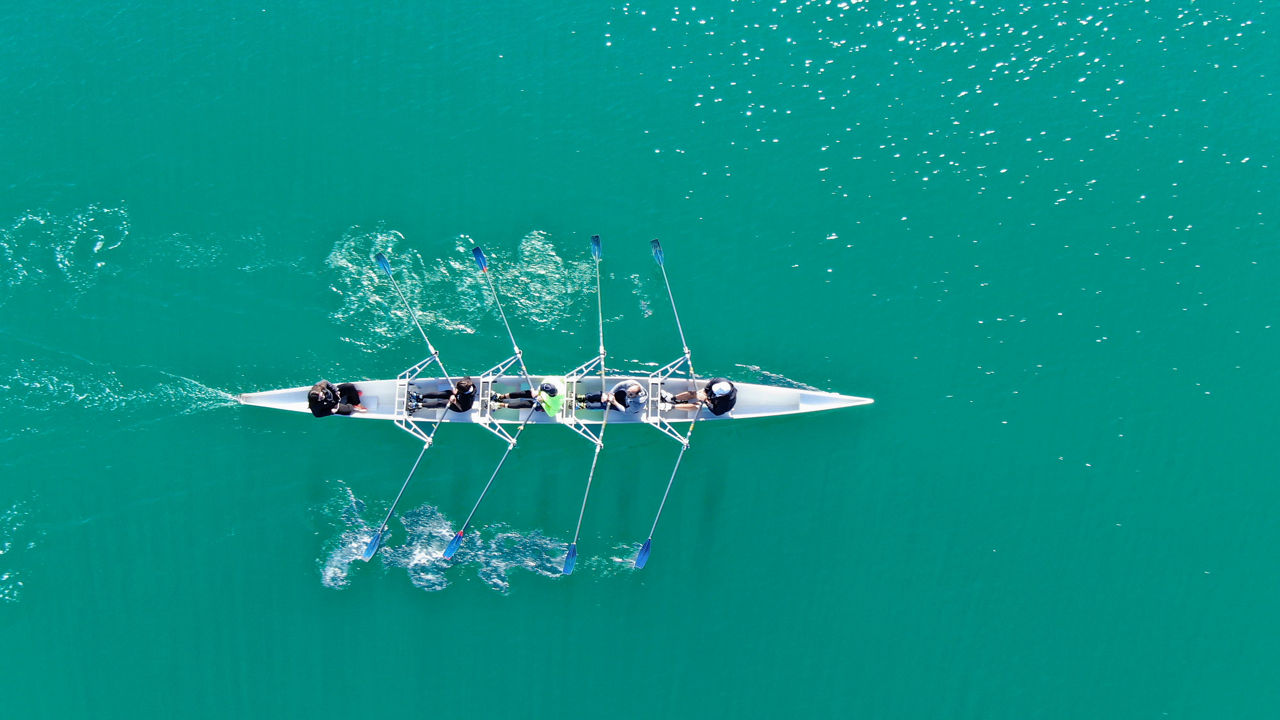Aerial drone top down photo of sport canoe operated by team of young women in emerald calm sea waters