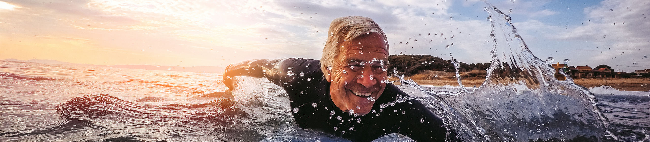 Active and happy senior man living to the fullest, surfing on a surfboard during his summer vacation 