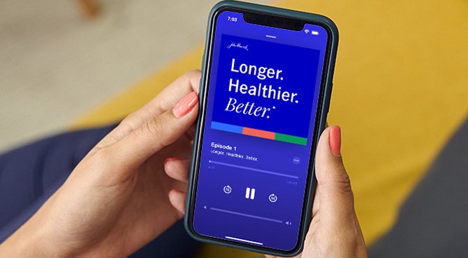 Woman holding a phone in her hand listening to a Longer. Healthier. Better. podcast episode