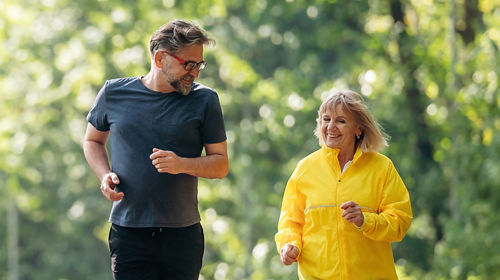Mature man and woman walking along trail in green space. 