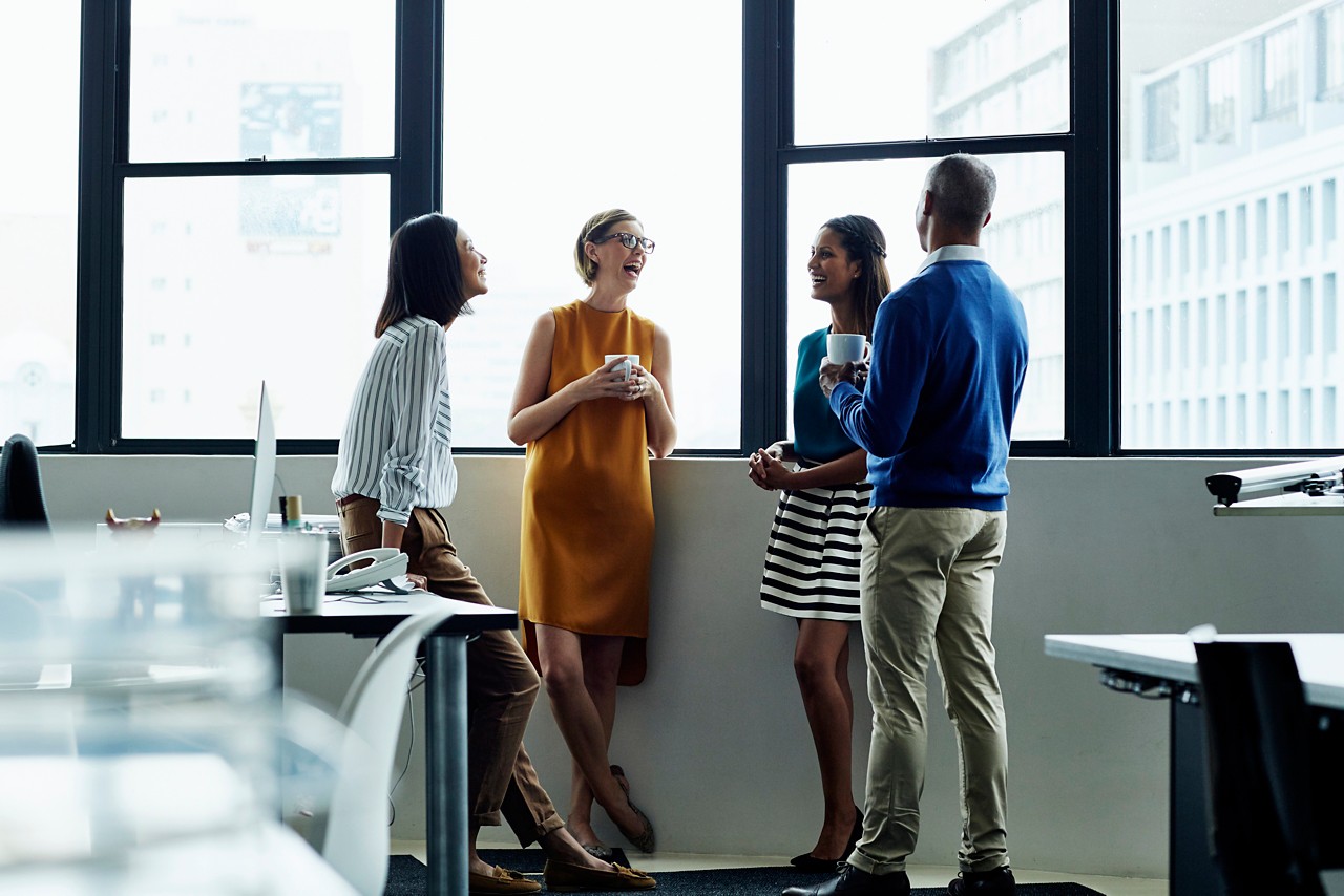 Cheerful multi-ethnic business people standing by office window during coffee break