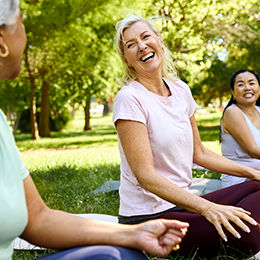 Trois femmes assises sur l’herbe dans un parc, en train de discuter.