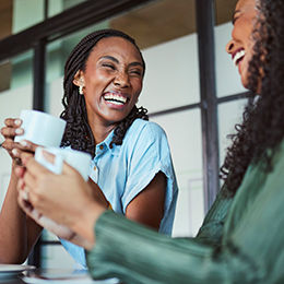Deux femmes tenant une tasse, en train de discuter et de rire.