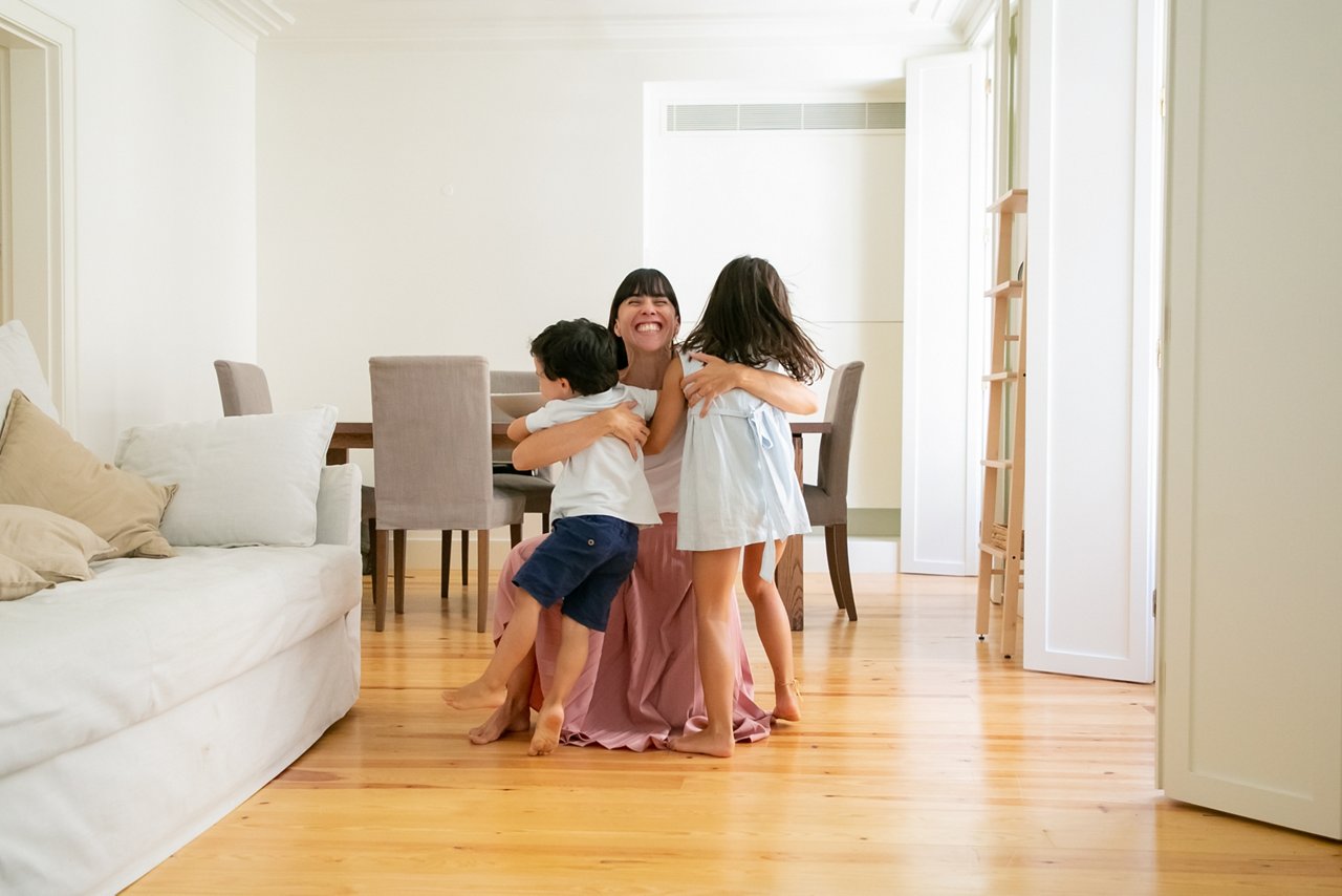 Laughing mother hugging adorable little kids at home. Happy pretty Caucasian mom embracing lovely children, smiling and playing with them. Motherhood, leisure and parenthood concept