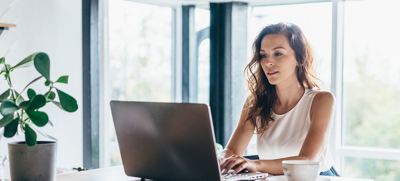 Une femme joyeuse travaille efficacement de chez elle, utilisant son ordinateur portable pour des tâches basées sur internet.