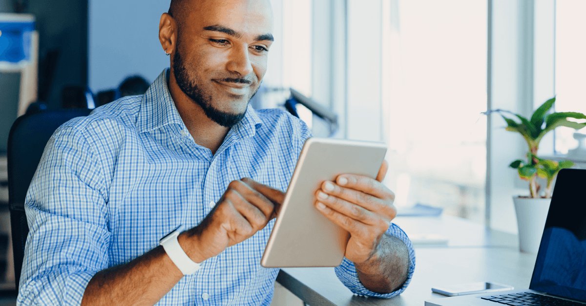 A business-savvy adult male, sitting at home with a warm coffee, is smiling as he works on his computer.