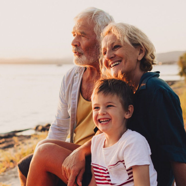 Older couple and a smiling child sit together by a lakeside.